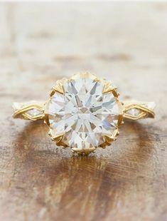 a yellow gold engagement ring with a round cut diamond in the center on a wooden surface