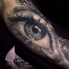 an eye tattoo on the arm with black and grey ink, which looks like it has been