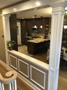 an open kitchen and dining room area in a house with hardwood floors, white columns, and dark wood cabinets