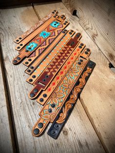 six leather guitar straps with designs on them sitting on a wooden table next to each other