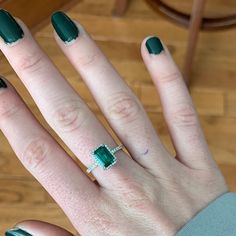 a woman's hand with green nail polish and an emerald ring on her finger