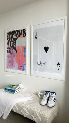 two paintings hang on the wall next to a bed with white sheets and blue sneakers