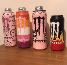 four monster energy drink cans are lined up on a wooden table in front of a wall