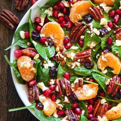 a white bowl filled with spinach salad topped with oranges and pecans