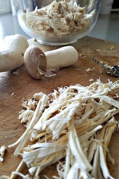 mushrooms and garlic on a cutting board next to a glass bowl filled with shredded cheese