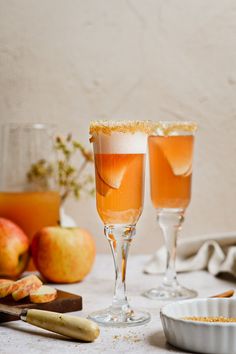 two glasses filled with orange liquid next to some apples