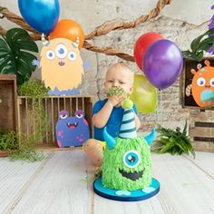 a baby is sitting in front of some balloons and eating something out of his mouth