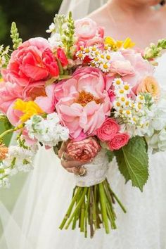 a bridal holding a bouquet of pink and yellow flowers with greenery in the background