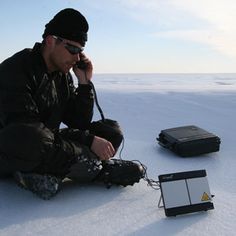 a man sitting in the snow talking on a cell phone next to an electronic device