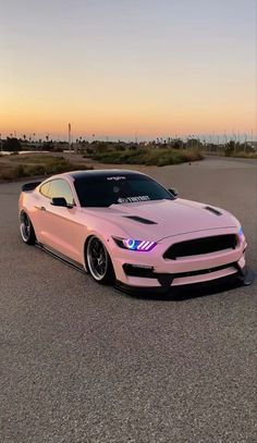 a pink mustang parked in a parking lot with the sun setting on it's side