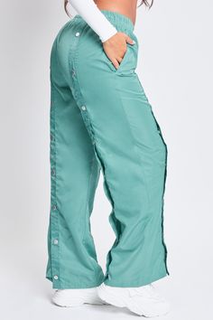 Off-duty vibes! Our Snap Wide Leg Pant is the perfect combination of parachute pants and track pants. These are great for days you want to rock a comfy and sporty look, but with a streetwear vibe. Featuring snap buttons centered along the fronts and backs of each leg for design and functional purposes. Not only do they look super trendy and chic, but you can unsnap or snap them to adjust the pants to the width of your liking. Also designed with an elastic waistband and drawstring for ultimate co Casual Pants With Button Closure For Streetwear, Casual Streetwear Pants With Button Closure, Relaxed Fit Bottoms With Button Closure For Streetwear, Urban Streetwear Bottoms With Button Closure, Stretch Utility Parachute Pants For Streetwear, Trendy Nylon Pants For Streetwear, Casual Bottoms With Buttons For Streetwear, Trendy Streetwear Pants With Button Closure, Casual Wide Leg Pants With Snap Buttons