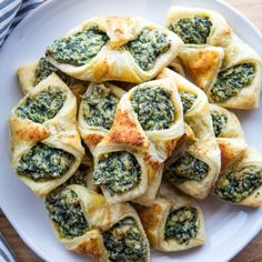 a white plate topped with spinach rolls on top of a wooden table next to a blue and white striped napkin