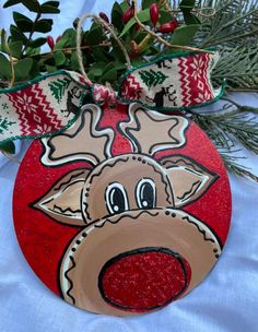 a red ornament with a reindeer face on it's head and green leaves