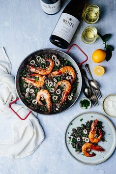 a pan filled with shrimp and rice next to two bottles of wine on top of a table