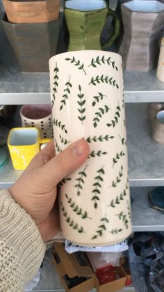 a hand holding a coffee cup with green leaves on it