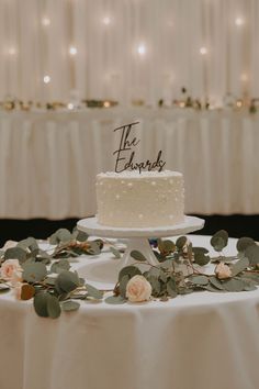 a white wedding cake sitting on top of a table covered in flowers and greenery