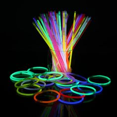 neon colored straws are in a glass vase on a reflective surface with black background