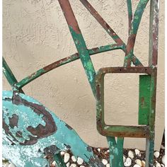 an old rusty metal chair sitting in front of a wall with rocks and pebbles on the ground