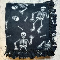 a black and white blanket with skeletons on it, fringe trim around the edges is laying on a marble surface