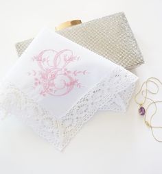 two napkins with pink designs on them next to some gold jewelry and a pair of earrings