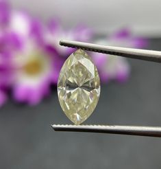 a close up of a diamond being held by a pair of tongs with purple flowers in the background