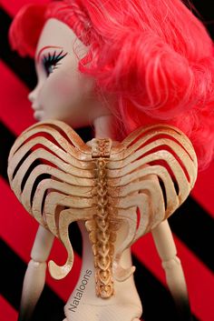 a doll with pink hair and gold chains on it's neck, standing in front of a black and red striped background