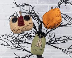 three handmade halloween ornaments hanging from a tree with branches in front of a brick wall