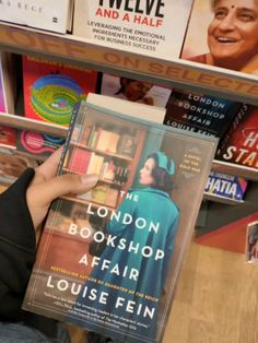 a person is holding up a book in front of bookshelves