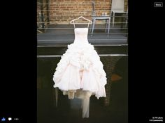 a wedding dress hanging on a rack in front of a brick wall with chairs around it