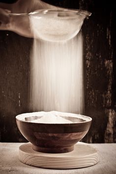 a wooden bowl is being sprinkled with white flour by a person's hand