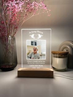 a vase with pink flowers in it sitting next to a candle and a photo frame