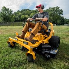 a man riding on the back of a yellow ride on a lawn mower in a field