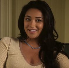 a woman sitting in a chair with a necklace on her neck and smiling at the camera