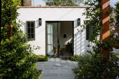 an open door to a small white house surrounded by greenery