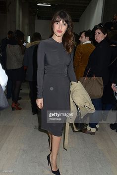 a woman standing in front of a group of people at an art exhibition, wearing a black