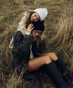 a woman sitting on the ground talking on her cell phone while wearing boots and a beanie