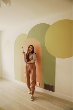 a woman standing in front of a wall with circles painted on it and holding a cell phone