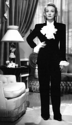 an old photo of a woman in a black suit and white shirt standing in a living room