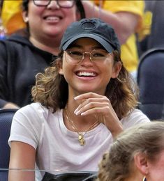 a woman sitting in the stands at a tennis game wearing glasses and a hat with her hand on her chin