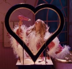 a woman holding a pink hairdryer in front of a heart shaped mirror