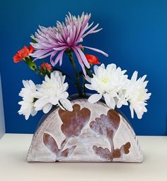 a vase with flowers in it sitting on a table next to a blue wall,