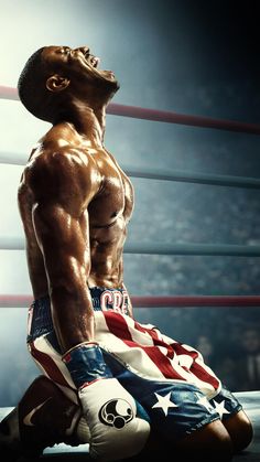 a man sitting on top of a boxing ring wearing shorts and an american flag shirt