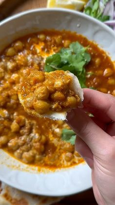 a hand holding a tortilla over a bowl of chili and beans with cilantro