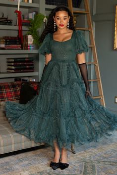 a woman in a green dress standing next to a couch with a ladder behind her