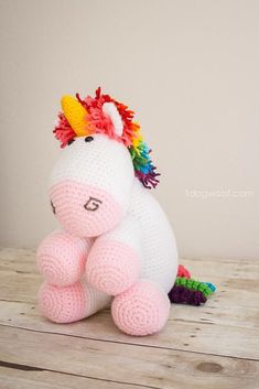 a crocheted stuffed unicorn sitting on top of a wooden table next to a white wall