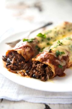 a white plate topped with meat and cheese enchiladas