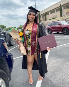 a woman in a graduation gown and cap is standing in the parking lot with her diploma