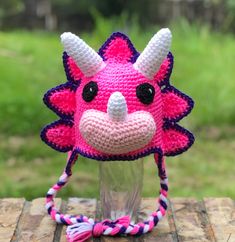 a crocheted pink and purple animal hat on top of a wooden table with grass in the background