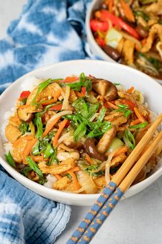 two white bowls filled with stir fry vegetables and rice next to chopsticks on a blue towel