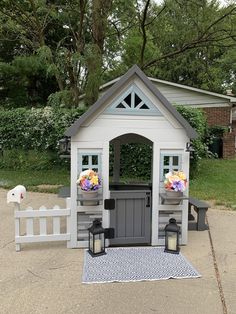 a small white gazebo with flowers and lanterns on the front door, next to a fence